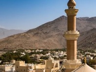 A scenic view of a mosque's minaret and dome overlooking a traditional village with a mountain backdrop.