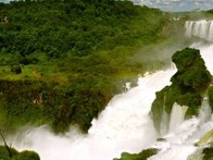 A panoramic view of a majestic waterfall surrounded by lush greenery under a cloudy sky.