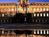 A classical building reflected in water at twilight with a clear sky.