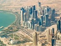 Aerial view of a modern cityscape near a large body of water, featuring tall skyscrapers and developed infrastructure.