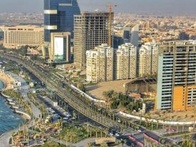 Aerial view of a modern coastal city with skyscrapers, a beach, and a distinctive building resembling a sail.