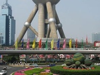 A view of the Shanghai Oriental Pearl Tower with colorful flags and neatly arranged flower beds in the foreground.