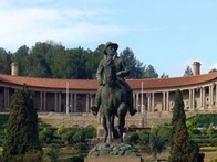 Statue of a man riding a horse in front of a classical building with landscaped gardens.