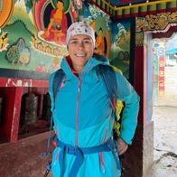 A person stands smiling in a colorful temple adorned with intricate paintings.