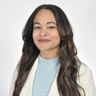 A portrait of a smiling woman with long curly hair, wearing a light blue turtleneck and a white blazer.