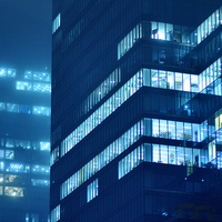 A night scene of modern buildings illuminated by blue lights in a foggy atmosphere.