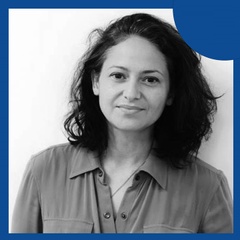 A monochrome photo of a woman in a collared shirt, with a plain background and a graphical blue element in the top right corner.