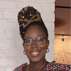 A smiling woman with glasses, wearing a floral top and a decorative headwrap.