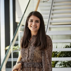 A woman in a patterned dress smiling while standing on stairs in a modern office building.