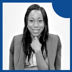 A professional smiling woman in a suit, with her hand on her chin, against a blue background.