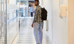 A young man wearing headphones stands in a corridor looking back over his shoulder.