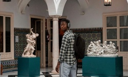 A young man wearing headphones stands in an art gallery surrounded by sculptures.