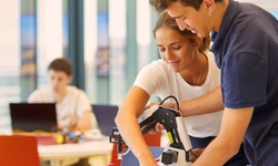 Two students are working together with a robotic arm in a classroom setting.