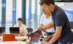 Two students are collaborating on a robotics project using a robotic arm.