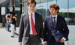 Two young men in business suits walking and conversing outdoors.