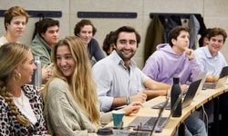 A group of students engaged in a classroom setting with laptops and casual interaction.