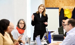A group of people engaged in a business discussion around a table, with one woman leading the conversation.
