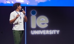 A speaker presenting on stage at an event for IE University.