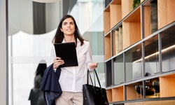 A professional woman walking in an office environment while holding a tablet.