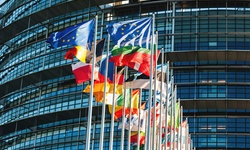 The image shows a row of flags in front of a modern building.