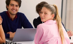 A group of young people engaged in a casual conversation around a laptop.