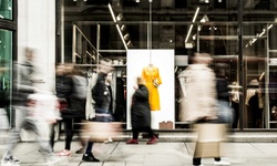Blurred figures walking past a fashion store display with a bright yellow jacket on a mannequin.