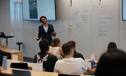 A man is presenting in front of a classroom while students listen attentively.