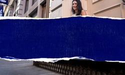 A woman stands outside a building with a torn blue banner in the foreground.