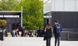 A couple walks together in a casual outdoor setting with people in the background.