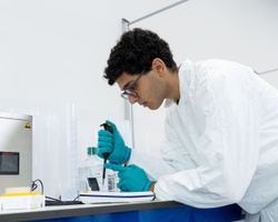 A researcher in a lab coat is using a micropipette to measure liquid in a laboratory setting.