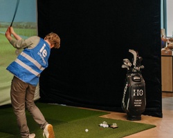 A person is golfing indoors, swinging a club in front of a simulator screen.