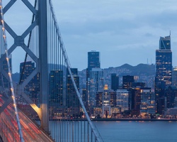 A scenic view of a city skyline with a bridge in the foreground at dusk.