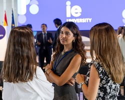 Three women are engaged in conversation at an academic event.