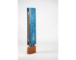A blue glass sculpture mounted on a wooden base against a white background.
