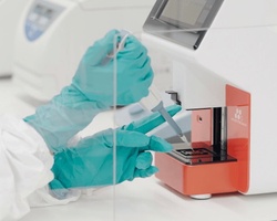 A person in protective gloves is using a laboratory device for testing.