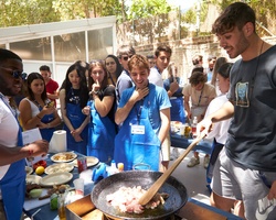 A lively outdoor cooking class with diverse participants engaging in food preparation.