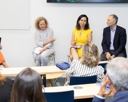 A group of professionals engages in a discussion in a meeting room, observed by an audience.
