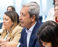 A mature man in a blue blazer attentively participates in a meeting surrounded by other professionals.