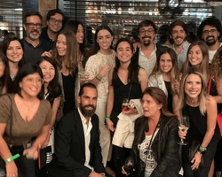 A group of people posing for a photo at a night event, smiling and holding drinks.