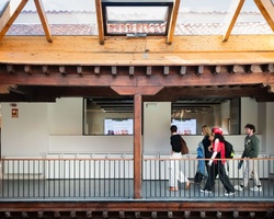 A modern exhibition space with people walking through it under a wooden structure.