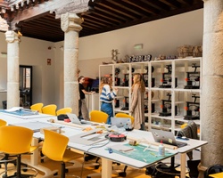 A modern workspace with people collaborating around tables and 3D printers in the background.