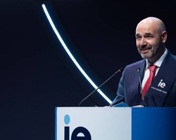 A man speaking at a podium with the letters 'IE' visible, surrounded by modern lighting design.