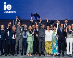 A group of people celebrating together at an event with IE University branding in the background.