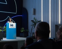 A speaker presents on stage at an event hosted by IE University.