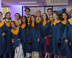 A group of graduates in blue and gold robes smiling at a graduation ceremony.
