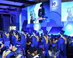 A graduation ceremony with students in blue and yellow caps and gowns listening to speakers on a stage.