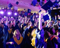 A large group of graduates celebrating and throwing their caps in the air at a graduation ceremony.