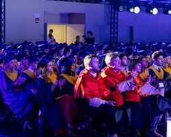 A group of graduates sitting in a ceremony wearing robes and caps.