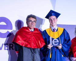 A graduate in a cap and gown stands proudly between two individuals, celebrating at a university event.