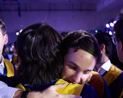 A moment of graduates celebrating together with hugs during their graduation ceremony.